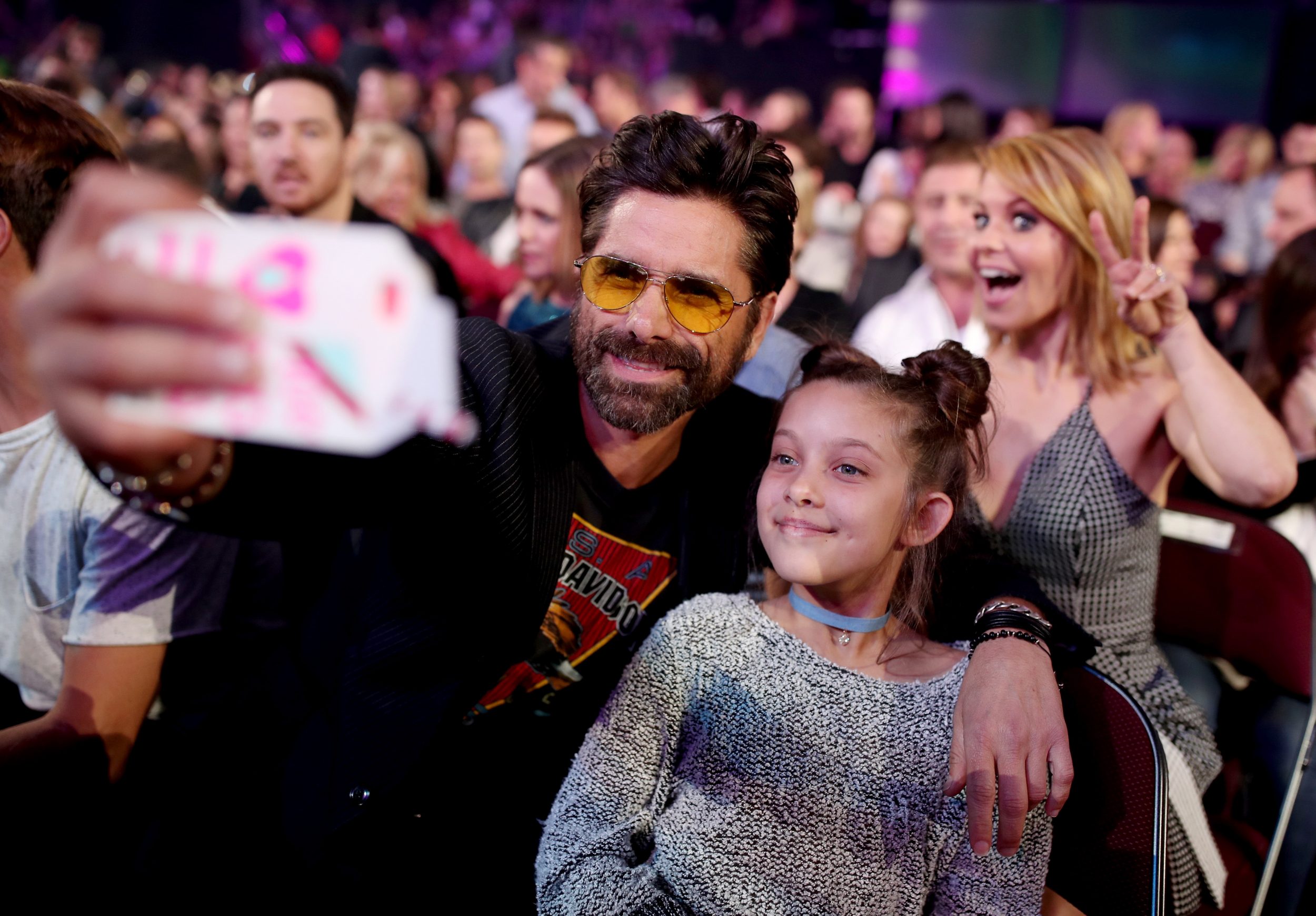 LOS ANGELES, CA - MARCH 11:  Actor John Stamos (L) takes a selfie with a fan while actor Candace Cameron Bure (R) photobombs at Nickelodeon's 2017 Kids' Choice Awards at USC Galen Center on March 11, 2017 in Los Angeles, California.  (Photo by Chris Polk/KCA2017/Getty Images for Nickelodeon)